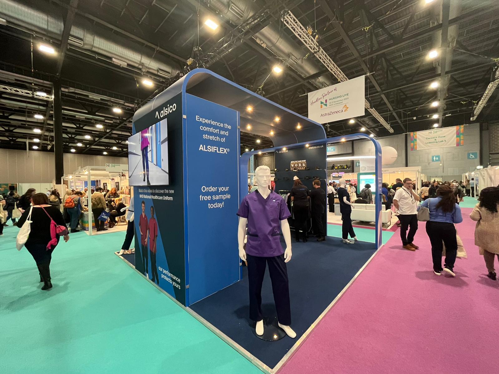 Alsico trade show stand at Nursing Live with mannequin wearing purple healthcare uniform.